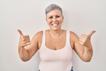 Sticker - Middle age caucasian woman standing over white background success sign doing positive gesture with hand, thumbs up smiling and happy. cheerful expression and winner gesture.