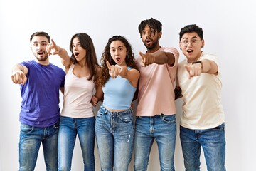 Poster - Group of young people standing together over isolated background pointing with finger surprised ahead, open mouth amazed expression, something on the front