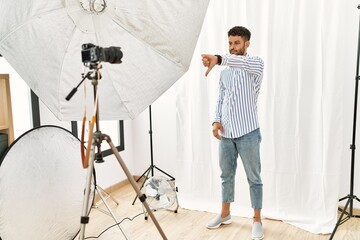 Canvas Print - Arab young man posing as model at photography studio looking unhappy and angry showing rejection and negative with thumbs down gesture. bad expression.