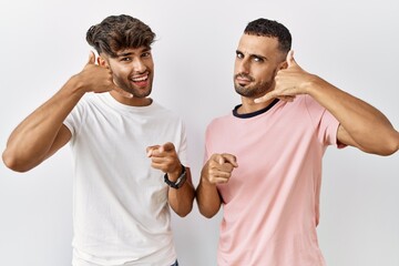 Sticker - Young gay couple standing over isolated background smiling doing talking on the telephone gesture and pointing to you. call me.