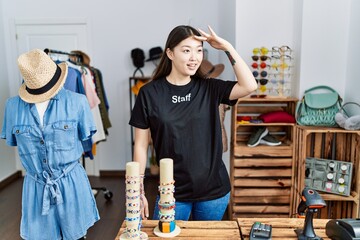 Wall Mural - Young asian woman working as manager at retail boutique very happy and smiling looking far away with hand over head. searching concept.