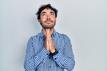 Wall Mural - Young hispanic man wearing casual clothes begging and praying with hands together with hope expression on face very emotional and worried. begging.