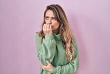 Young Caucasian Woman Standing Over Pink Background Looking Stressed And Nervous With Hands On Mouth Biting Nails. Anxiety Problem.