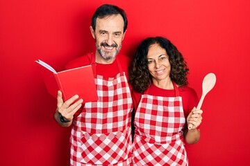 Canvas Print - Middle age couple of hispanic woman and man wearing professional apron reading cooking recipe book smiling with a happy and cool smile on face. showing teeth.