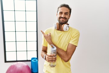 Sticker - Young hispanic man wearing sportswear and drinking water at the gym pointing aside worried and nervous with forefinger, concerned and surprised expression