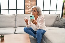 Middle age woman using smartphone holding pills at home