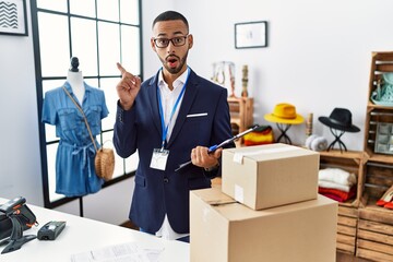 Poster - African american man working as manager at retail boutique surprised pointing with finger to the side, open mouth amazed expression.