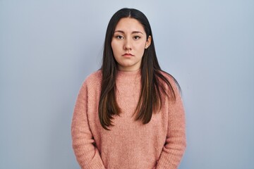 Sticker - Young latin woman standing over blue background relaxed with serious expression on face. simple and natural looking at the camera.