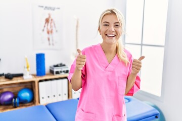 Poster - Young caucasian woman working at pain recovery clinic success sign doing positive gesture with hand, thumbs up smiling and happy. cheerful expression and winner gesture.