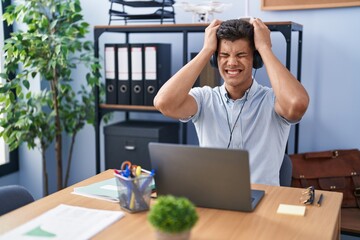 Sticker - Young hispanic man working at the office wearing headphones suffering from headache desperate and stressed because pain and migraine. hands on head.