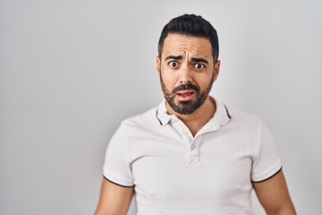 Canvas Print - Young hispanic man with beard wearing casual clothes over white background in shock face, looking skeptical and sarcastic, surprised with open mouth