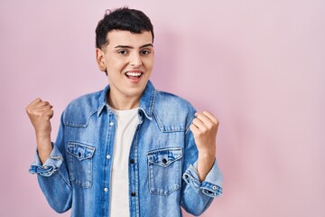 Wall Mural - Non binary person standing over pink background screaming proud, celebrating victory and success very excited with raised arms