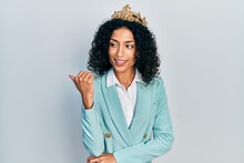 Young Latin Girl Wearing Business Clothes And Queen Crown Smiling With Happy Face Looking And Pointing To The Side With Thumb Up.