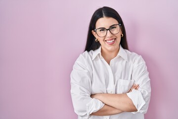 Sticker - Young brunette woman standing over pink background happy face smiling with crossed arms looking at the camera. positive person.