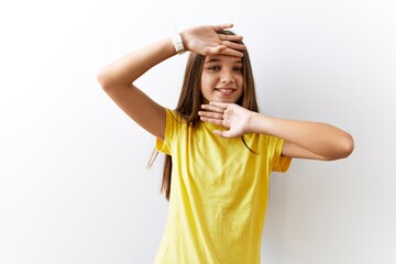 Poster - Young brunette teenager standing together over isolated background smiling cheerful playing peek a boo with hands showing face. surprised and exited