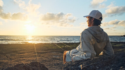 Man on a beach is looking distance during beautiful summer sunset. Human looks to the sun over horizon in the morning while sunrise. Happy person contemplates the beauty of nature. Freedom concept.