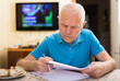 © caftor - Elderly man writes a letter on a sheet of paper while sitting at a table in room