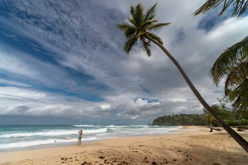 Wall Mural - Girl with palms at the beach of Playa Grande Rio San Juan under cloudy sky, Dominican Republic