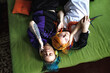 Portrait of a young tattooed punk couple of a girl and a guy with long dyed hair braided, lying on a large green bed, top view. They listen to music.