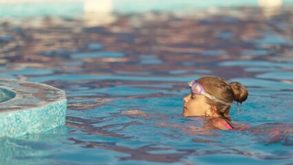 Canvas Print - A girl in a bright swimsuit with swimming goggles dives into a pool with clear transparent water