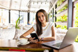 © F8  \ Suport Ukraine - Portrait image of a young woman holding and using mobile phone and laptop in cafe