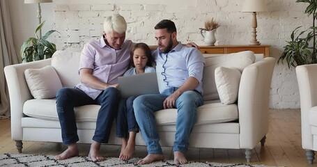 Wall Mural - Engaged gen Z boy, grandpa and dad using laptop on home couch together, talking, playing virtual game, discussing videogame, speaking on video call, smiling, laughing. Communication concept