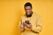 © gstockstudio - Handsome African man with headphones using smart phone while standing against yellow
