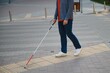 © Serhii - young blind man with white cane walking across the street in city