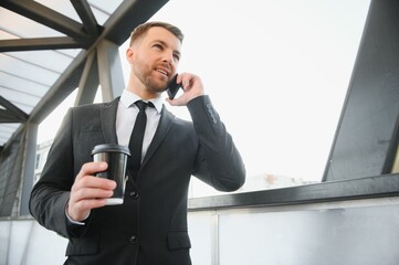 Bearded businessman in formal suit on break using mobile phone use smartphone. business man standing outside on modern urban city street background with coffee cup in downtown outdoors. copy space