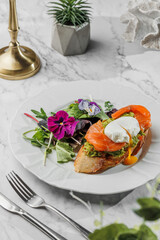 Wall Mural - Bruschetta with Poached egg and fresh salmon , vegetarian salad with greens at the white plate on light marble background. Healthy sea food, hard light, restaurant decor