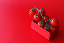 Branch Red Baby Plum Tomatoes In A Red Paper Box On A Red Background.