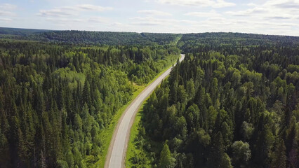 Aerial view of white car driving on country road in forest. Aerial view flying over old patched two lane forest road with car moving green trees of dense woods growing both sides. Car driving along