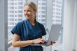 © Yaroslav Astakhov - Smiling female healthcare worker using laptop while working at doctor's office and looking window