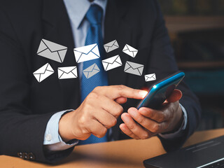 Wall Mural - businessman holding a smartphone receives a new message with email icons while sitting in the office