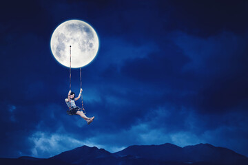 woman sit on the swing while hanging on moon