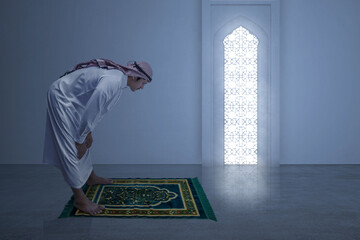 Wall Mural - Muslim man with keffiyeh with agal in praying position (salat) on the prayer rug