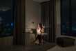 © shine - Work and travel. Young Asian traveler using laptop on table at the lamp with making video call meeting to team online in hotel room at night during a summer vacation holiday travel and suitcase on bed
