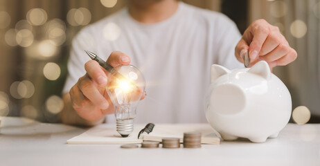 Poster - business man hand holding lightbulb and putting coin in to the piggy bank. idea saving energy and accounting finance in home and family concept, save world and energy power.