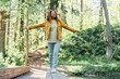 © Westend61 - Smiling woman with arms outstretched walking on wooden plank in forest