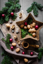 Studio Shot Of Cutting Board, Star Shaped Wicker Basket, Twigs, Christmas Ornaments, Walnuts And Simple Nutcracker