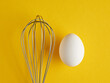 A whisker and a white egg on yellow background. Whisk cooking egg beater mixer whisker.
