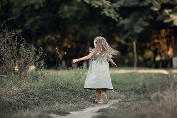 Wall Mural - beautiful little girl with long hair plays, spins in a dress. Walk in the park, summer vacation, concept of family vacation, leisure and outdoor activities.