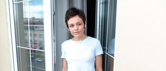 A model with a short haircut enjoys the morning on the balcony. A young woman with headphones listening to music