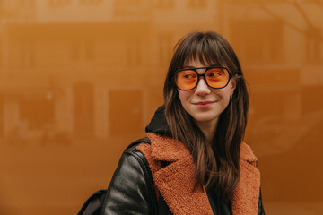 Portrait of smiling woman with black backpack and orange sunglasses .