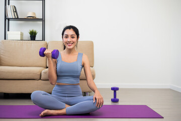 Wall Mural - Attractive asian young fitness woman lifting dumbbell weights workout at home in living room. Fresh feeling female training and exercise wearing sport wear fit body.