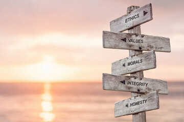 ethics values morals integrity honesty  text engraved on wooden signpost at the beach during sunset.