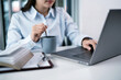 © Charlie's - Asian Business woman drinking coffee and working on laptop computer while sitting at office. holding cup of coffee Achievement business career concept.