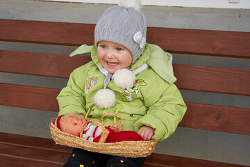 happy little girl with a doll on the bench,toddler girl in a jacket sitting on a bench with a doll