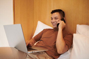 Wall Mural - Young man talking on phone with colleague or client when working on laptop