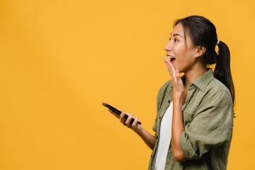 Wall Mural - Young Asia lady using phone with positive expression, smiles broadly, dressed in casual clothing feeling happiness and stand isolated on yellow background. Happy adorable glad woman rejoices success.